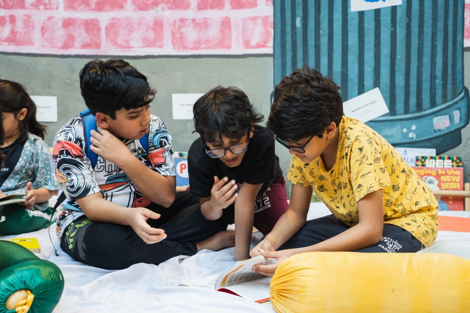 Three boys huddled over a book on the floor in front of a mural
