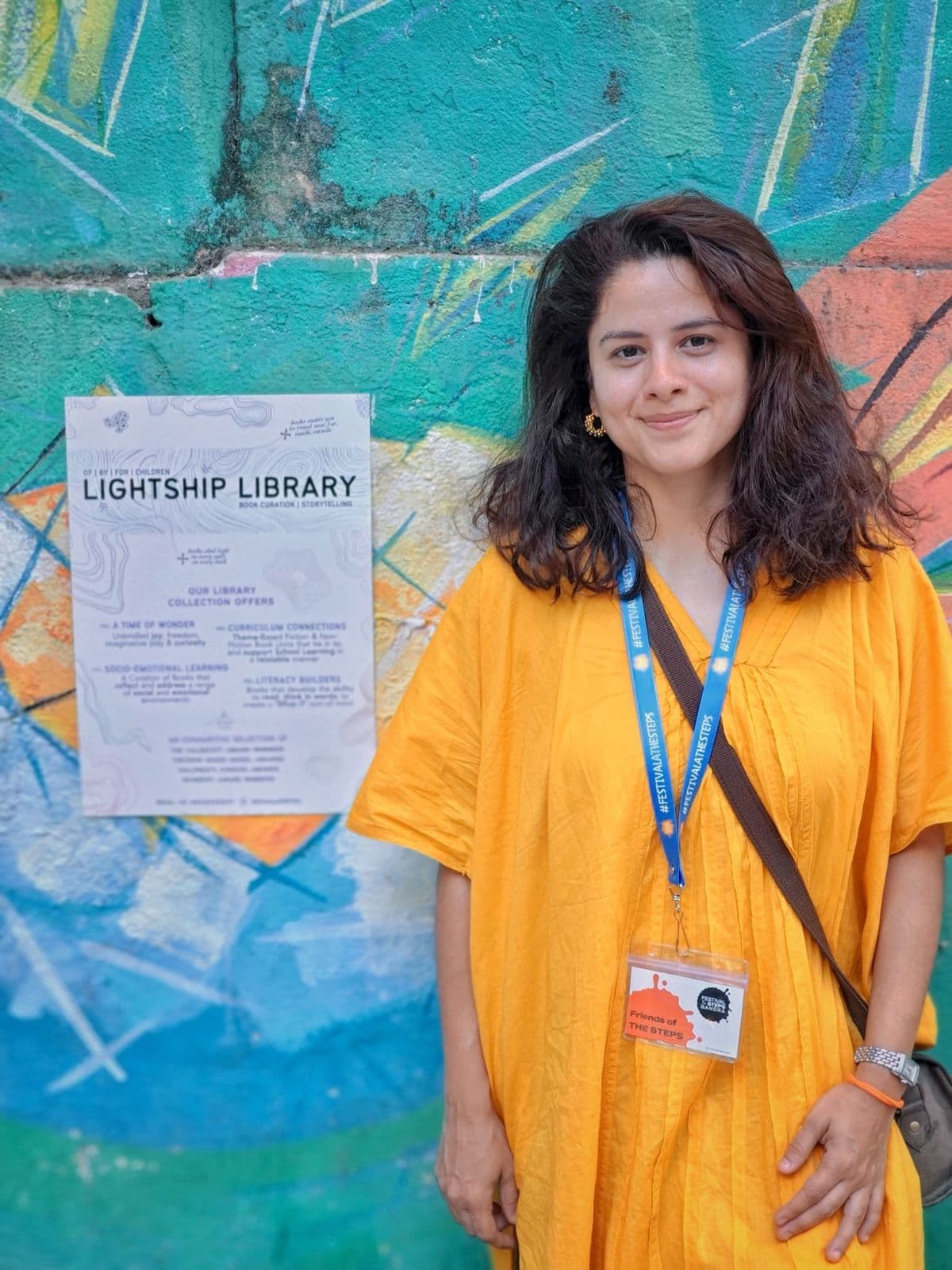 Neha Aurora, founder of Lightship, standing in front of a colourful mural wearing a Lightship lanyard